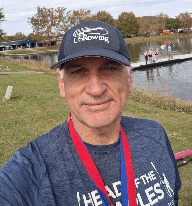 Trevor de Koekkoek at a rowing regatta, wearing a USRowing cap and Head of the Charles medal